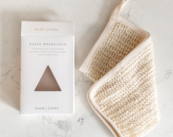 Puede incluir: Una caja blanca con el texto "NASH | JONES" y "AGAVE WASHCLOTH" junto a un paño de lavado beige. El paño de lavado está hecho de un material tejido con un lazo para colgar. La caja tiene un recorte triangular.
