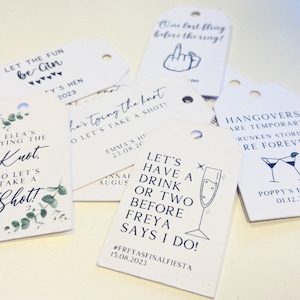 May include: A set of ten white gift tags with black ink. The tags feature various phrases related to a hen party, including "Let's have a drink or two before Freya says I do!" and "Hangover's are temporary, drunken stories are forever."