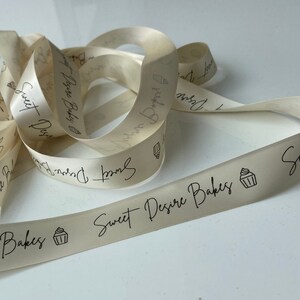 May include: A close-up of a white satin ribbon with the text "Sweet Desire Bakes" and a small cupcake icon printed on it.