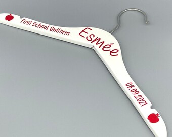 May include: White wooden hanger with a red apple design and the text "First School Uniform" and "Esmeé 05.09.2021".