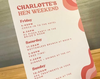 May include: A pink and white card with the text "Charlotte's Hen Weekend" in a bold, orange font. The card lists a weekend itinerary with activities and times for each day, including a bottomless brunch, a PJ pizza party, and spa treatments.