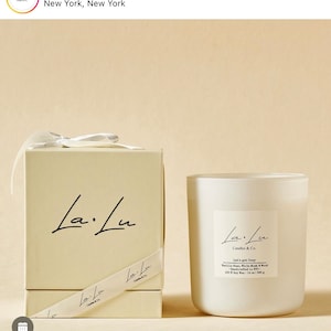 May include: A white candle jar with a white lid and a white box. The candle jar has a black label with the text "La.Lu Candles & Co. Let's get Cozy Vanilla Bean, White Musk & Wood Handcrafted in NYC 100g Soy Wax - 16 oz | 350g"