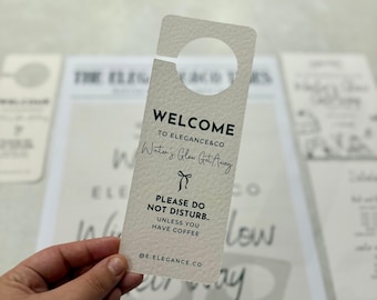 May include: A white door hanger with a circular cutout at the top. The text on the door hanger reads "WELCOME TO ELEGANCE&CO Winter's Glow Get Away PLEASE DO NOT DISTURB.. UNLESS YOU HAVE COFFEE @E.ELEGANCE.CO".