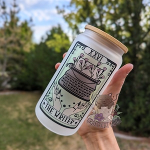 May include: White frosted glass water bottle with a bamboo lid. The bottle has a green and black illustration of a typewriter with flowers and the text "The Writer" and "XXVI". The bottom of the bottle has the text "Craftycat Mugs".