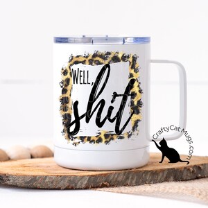 May include: White travel mug with a black and gold leopard print design and the text "Well, shit". The mug has a black cat silhouette on the side with the text "CraftyCat Mugs.com".