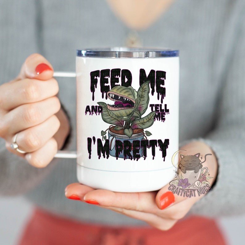 May include: White stainless steel travel mug with a black and green graphic of a plant with a mouth and the text "Feed Me And Tell Me I'm Pretty".
