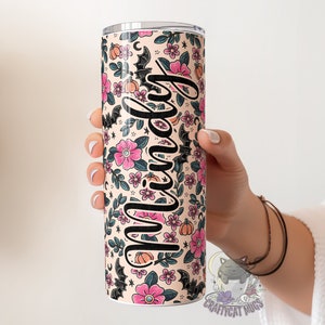 May include: A personalised stainless steel tumbler with a floral and bat pattern in pink, black and orange. The tumbler has the name "Mindy" written on it.