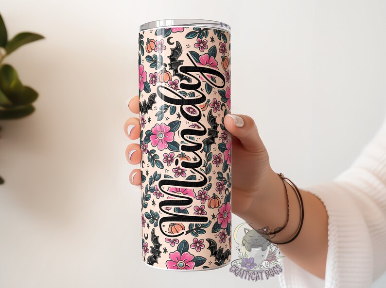 May include: A personalised stainless steel tumbler with a floral and bat pattern in pink, black and orange. The tumbler has the name "Mindy" written on it.