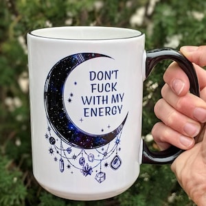 15oz coffee mug has a beautiful dark blue and black moon with crystals hanging down and the phrase 'don't fuck with my energy' on it.