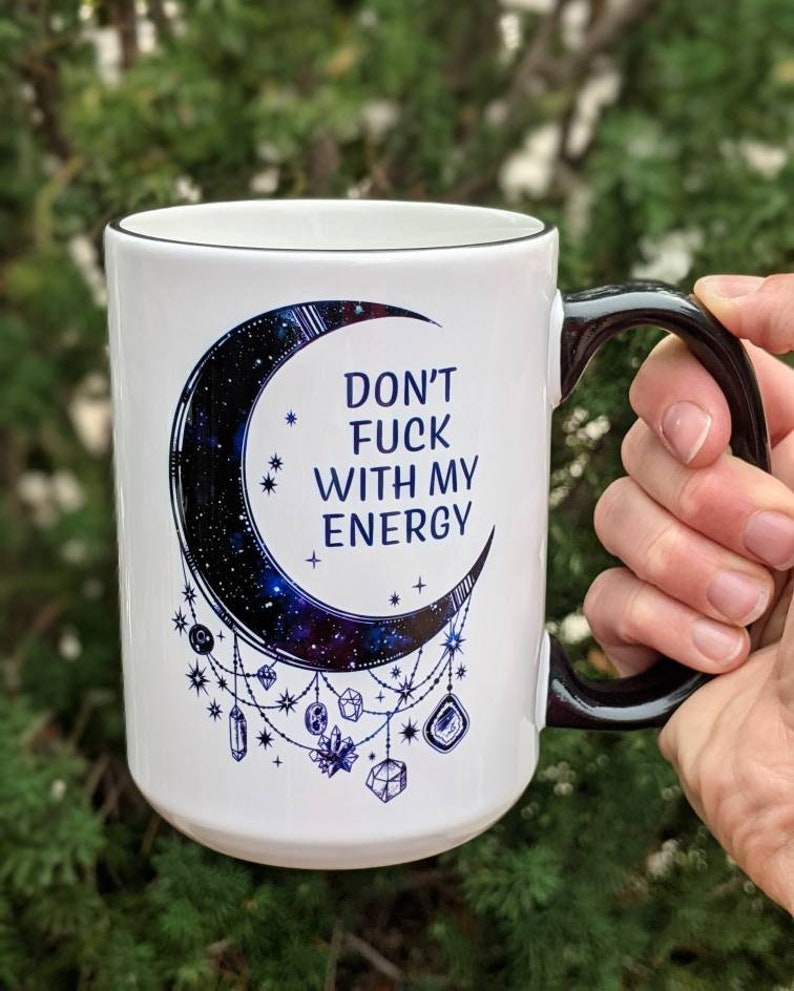 15oz coffee mug has a beautiful dark blue and black moon with crystals hanging down and the phrase 'don't fuck with my energy' on it.