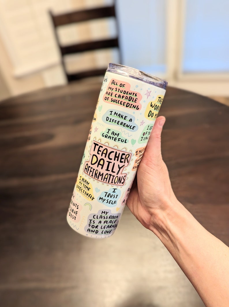 Op de afbeelding: Een witte roestvrijstalen tumbler met een kleurrijk ontwerp met de tekst "Teacher Daily Affirmations". De tumbler is bedekt met kleurrijke spraakballonnen met positieve affirmaties voor leraren, zoals "Al mijn leerlingen zijn in staat om te slagen", "Ik maak een verschil", "Ik ben dankbaar", "Ik plan mijn tijd effectief", "Ik vertrouw op mezelf", en "Mijn klaslokaal is een plek om te leren en te liefhebben".