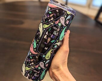 May include: A black and white tumbler with a spooky design featuring ghosts, stars, and a crescent moon. The tumbler has a colorful pattern of pastel green, pink, and purple ghosts.