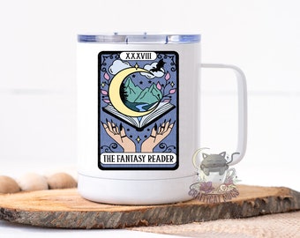 May include: White travel mug featuring a black and white illustration of a tarot card. The card is labelled "XXXVIII THE FANTASY READER" and depicts a crescent moon, a book, and two hands with long nails.