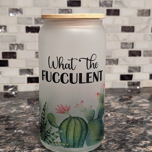 May include: A frosted glass jar with a bamboo lid and a cactus design. The jar has the text "What the FUCculent" printed on it.