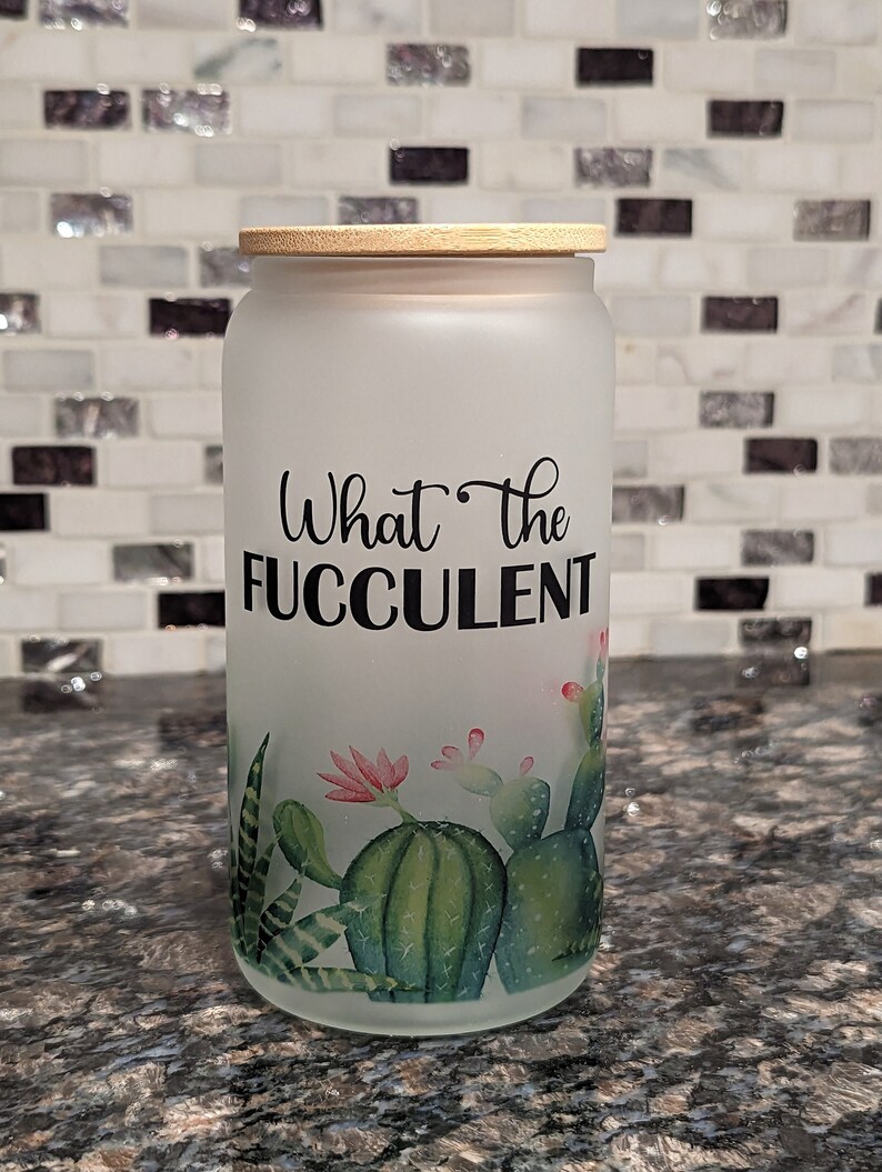 May include: A frosted glass jar with a bamboo lid and a cactus design. The jar has the text "What the FUCculent" printed on it.