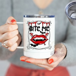 K&ouml;nnte beinhalten: Wei&szlig;e Edelstahl-Reisebecher mit einer schwarzen und roten Grafik eines Vampirmundes mit Z&auml;hnen und dem Text "Bite Me". Der Becher hat einen durchsichtigen Deckel mit einem schwarzen Schieberegler.
