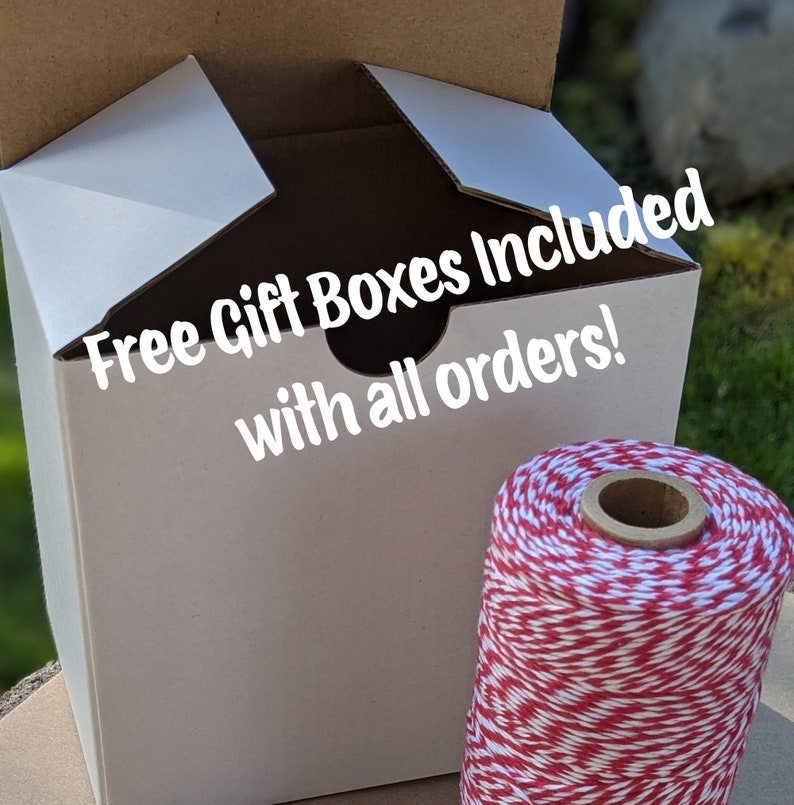 K&ouml;nnte beinhalten: Wei&szlig;e Geschenkschachtel aus Pappe mit dem Text "Free Gift Boxes Included with all orders!" auf der Vorderseite. Die Schachtel ist ge&ouml;ffnet und eine Spule roter und wei&szlig;er B&auml;ckergarn befindet sich im Vordergrund.