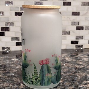 May include: A frosted glass jar with a bamboo lid and a cactus design. The jar has the word "Plant" written on it.