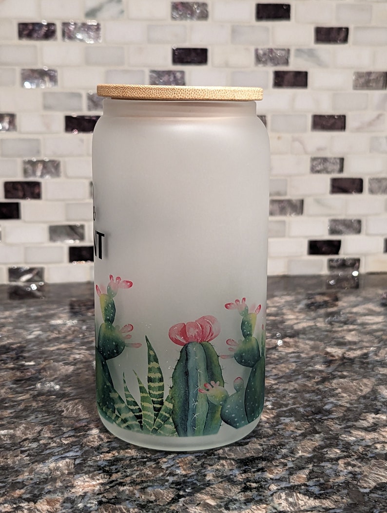 May include: A frosted glass jar with a bamboo lid and a cactus design. The jar has the word "Plant" written on it.