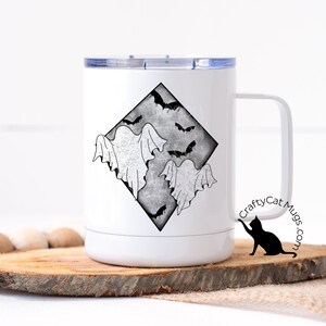 May include: White stainless steel travel mug with a black and white graphic of ghosts and bats in a diamond shape. The mug has a black lid and a black handle. The text "CraftyCat Mugs.com" is printed on the side of the mug.