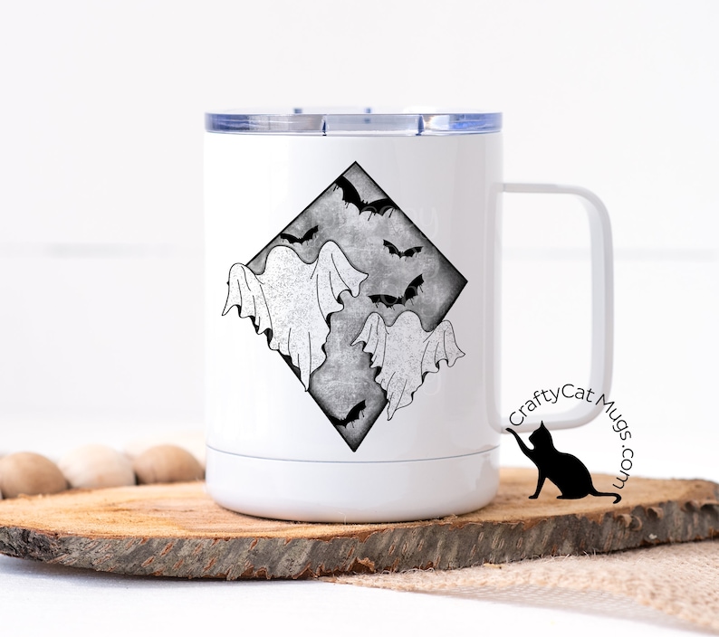 May include: White stainless steel travel mug with a black and white graphic of ghosts and bats in a diamond shape. The mug has a black lid and a black handle. The text "CraftyCat Mugs.com" is printed on the side of the mug.