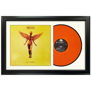 May include: A framed record album with a black frame and a white mat. The album cover features a yellow background with a figure with wings and the text "NIRVANA IN UTERO". The record is orange.
