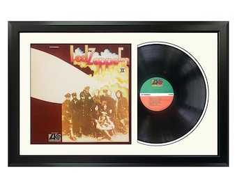 May include: A framed black vinyl record with a black and white album cover featuring a band of seven people standing in front of a white blimp. The album cover has the text "Led Zeppelin II" in orange and yellow letters. The record label is green and white with the text "Atlantic" in white letters.