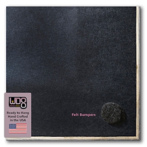 May include: A black chalkboard with a wood frame. The chalkboard has a white label with the text "Ready to Hang Hand Crafted in the USA" and an American flag. The chalkboard also has a black felt bumper on the bottom right corner. The text "Felt Bumpers" is printed in pink below the bumper.
