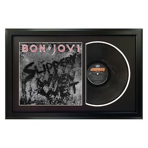 May include: A framed black vinyl record with a black and white album cover. The album cover features the text "BON JOVI" and "SLIPPERY WHEN WET".