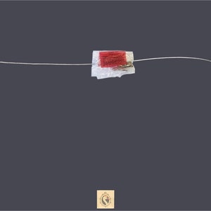 May include: A silver wire cable with a red and white label attached to it. The cable has a small silver connector on each end.