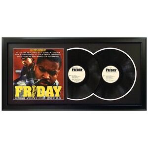 May include: A black framed double LP record display featuring the Friday movie soundtrack album cover. The cover features Ice Cube and Chris Tucker. The album title "Friday" is in large yellow letters. The record labels are visible with the title "Friday" printed on them.