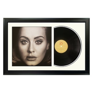 May include: A framed black vinyl record with a black and white photo of Adele on the album cover. The album cover has the title "25" in red text.