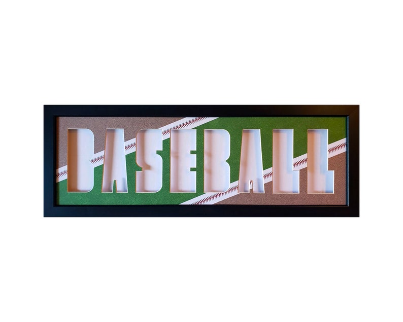 May include: A black framed wall decor with the word "BASEBALL" cut out of the center. The background is a brown and green baseball field pattern.