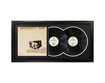 May include: A framed double LP record set of "Tusk" by Fleetwood Mac. The album cover features a black and white photo of a dog. The record labels are visible in the frame.