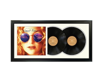 May include: A framed double LP record set of the soundtrack to the movie "Almost Famous". The album cover features a woman wearing sunglasses with a cityscape reflected in the lenses. The title "Almost Famous" is printed in white on a black background.
