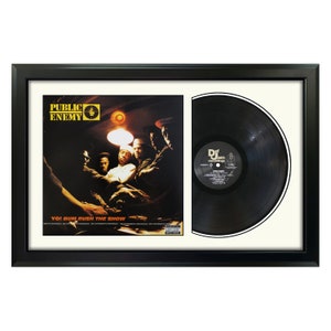 May include: A framed black vinyl record with a black and white album cover. The album cover features a group of men in a dimly lit room. The album cover text reads "Public Enemy" and "Yo! Bum Rush The Show".
