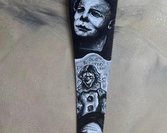 May include: A hand-painted saw blade with black and white images of horror movie characters. The characters include Michael Myers, Pennywise the Dancing Clown, and Freddy Krueger. The saw blade has the text "Our Beloved" and "Dreamers" on it.