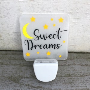 May include: A white night light with a frosted square panel featuring a yellow crescent moon, yellow stars, and the text "Sweet Dreams".