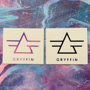 May include: Two square stickers with the Gryffin logo. The logo is a stylized triangle with wings. One sticker has a pink and purple gradient triangle, the other is black.