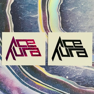 May include: Two stickers with the word "Ace Aura" in a stylized font. One sticker is pink and the other is black.