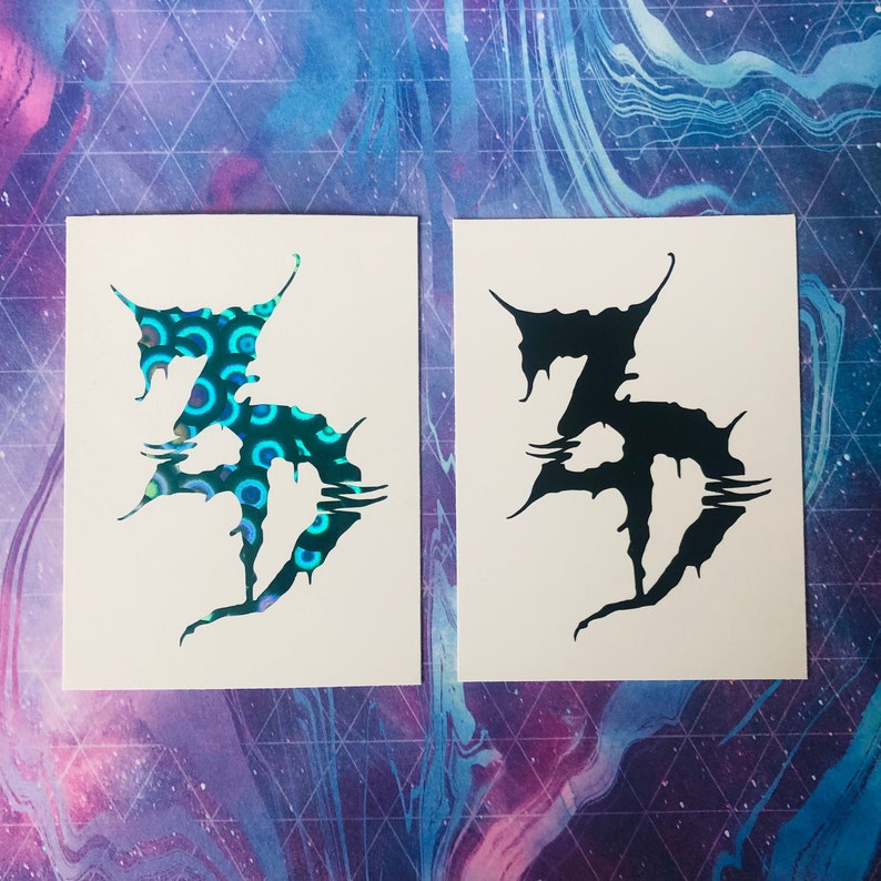 K&ouml;nnte beinhalten: Zwei wei&szlig;e Aufkleber mit einer schwarzen Grafik des Buchstabens "Z" mit einem stilisierten Tropfeffekt. Der linke Aufkleber hat einen holografischen Effekt mit einem blauen und gr&uuml;nen Muster.