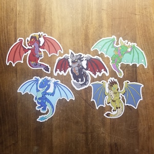 May include: Five colorful cartoon dragon stickers with wings outstretched. The dragons are red, green, gray, blue, and yellow.