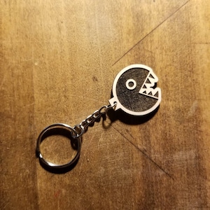 May include: A black and white wooden keychain shaped like a Pac-Man character with a silver metal ring.