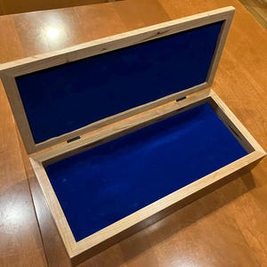 May include: A wooden box with a hinged lid, lined with blue velvet. The box is made of light wood with a natural finish.