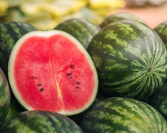 May include: A close-up of several watermelons, one cut in half. The cut watermelon reveals bright red flesh with black seeds. The whole watermelons have green and dark green striped rinds.