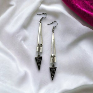 Puede incluir: Un par de pendientes de plata con un dise&ntilde;o triangular. Los pendientes tienen un patr&oacute;n geom&eacute;trico negro y cuentas blancas.