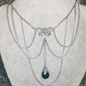 May include: A silver layered chain necklace with a black teardrop pendant. The pendant has a silver filigree design.