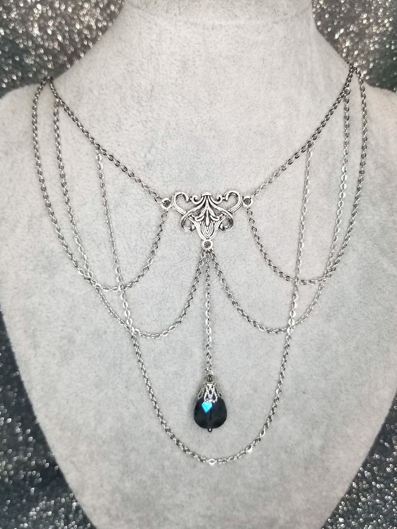 May include: A silver layered chain necklace with a black teardrop pendant. The pendant has a silver filigree design.