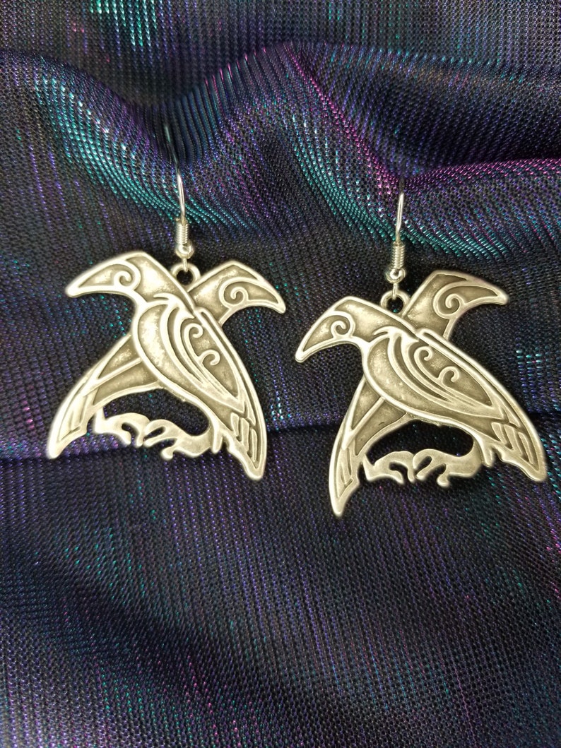 May include: A pair of silver earrings featuring a detailed design of a bird with intricate patterns. The earrings are hanging from silver hooks.