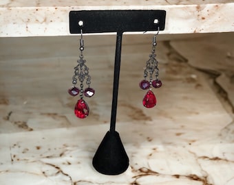 May include: A pair of dangle earrings with a black metal design and red and purple glass beads.